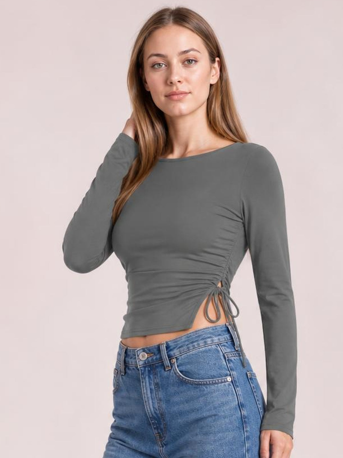 Model in a gray long-sleeve round-neck T-shirt with a fitted silhouette, ruched sides, and tied drawstring slit detail at the waist.