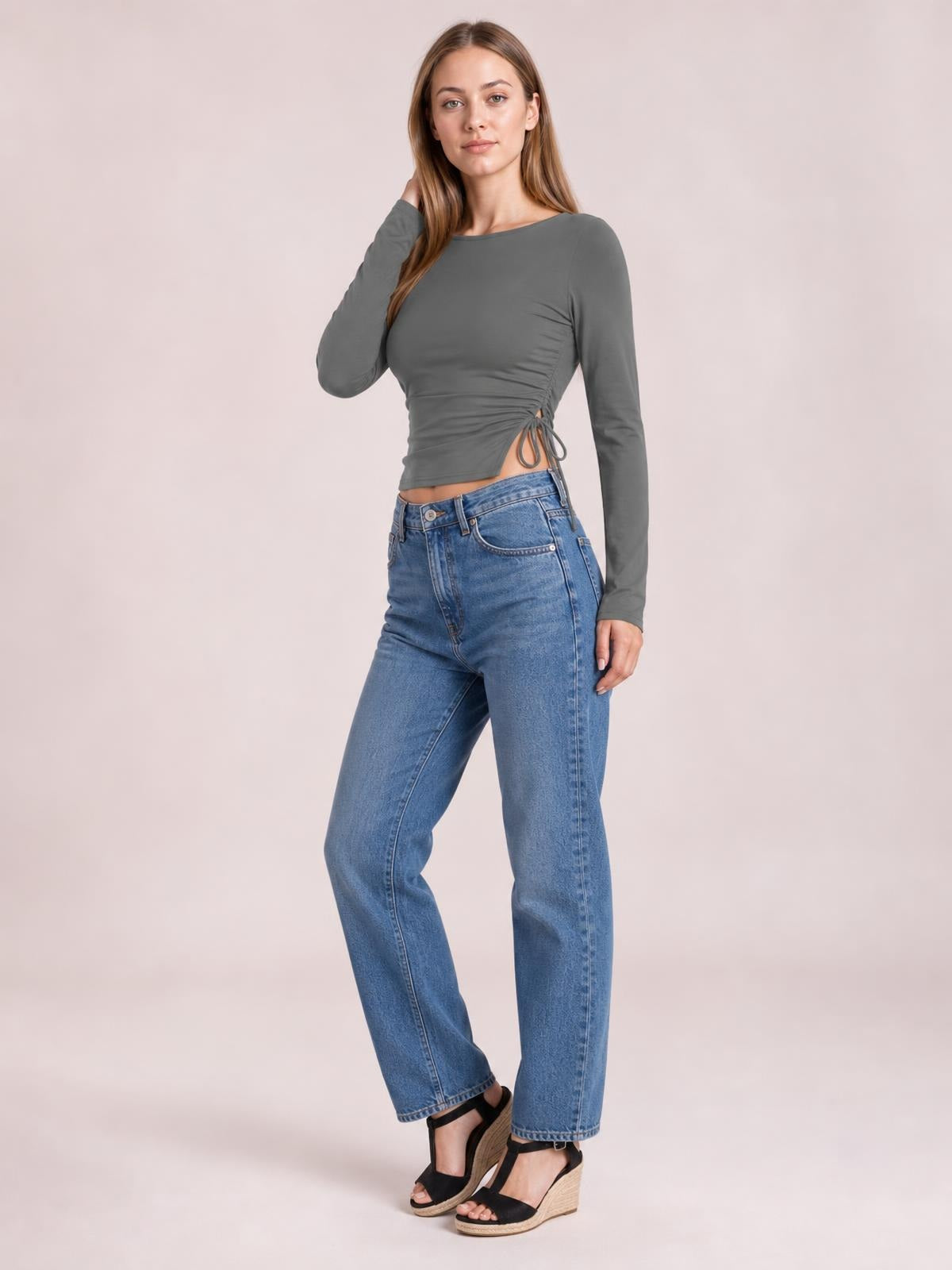 Model poses in a fitted charcoal gray round-neck long-sleeve T-shirt with ruched sides and a tied slit detail creating a cropped silhouette.