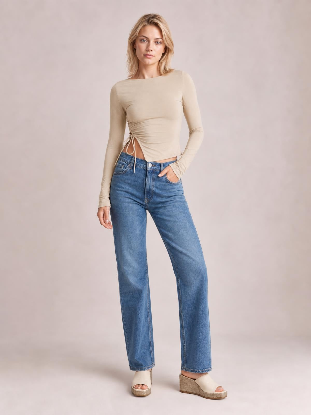 A model poses in a fitted beige tied slit round-neck long-sleeve T-shirt with side ruching and dangling ties at the waist.