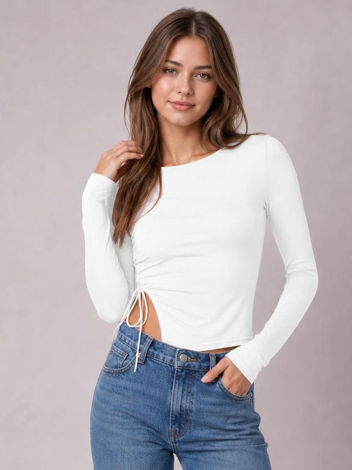 Model poses in a fitted white round-neck long-sleeve T-shirt with a tied side slit, gathered waist detail, and slightly stretchy silhouette.