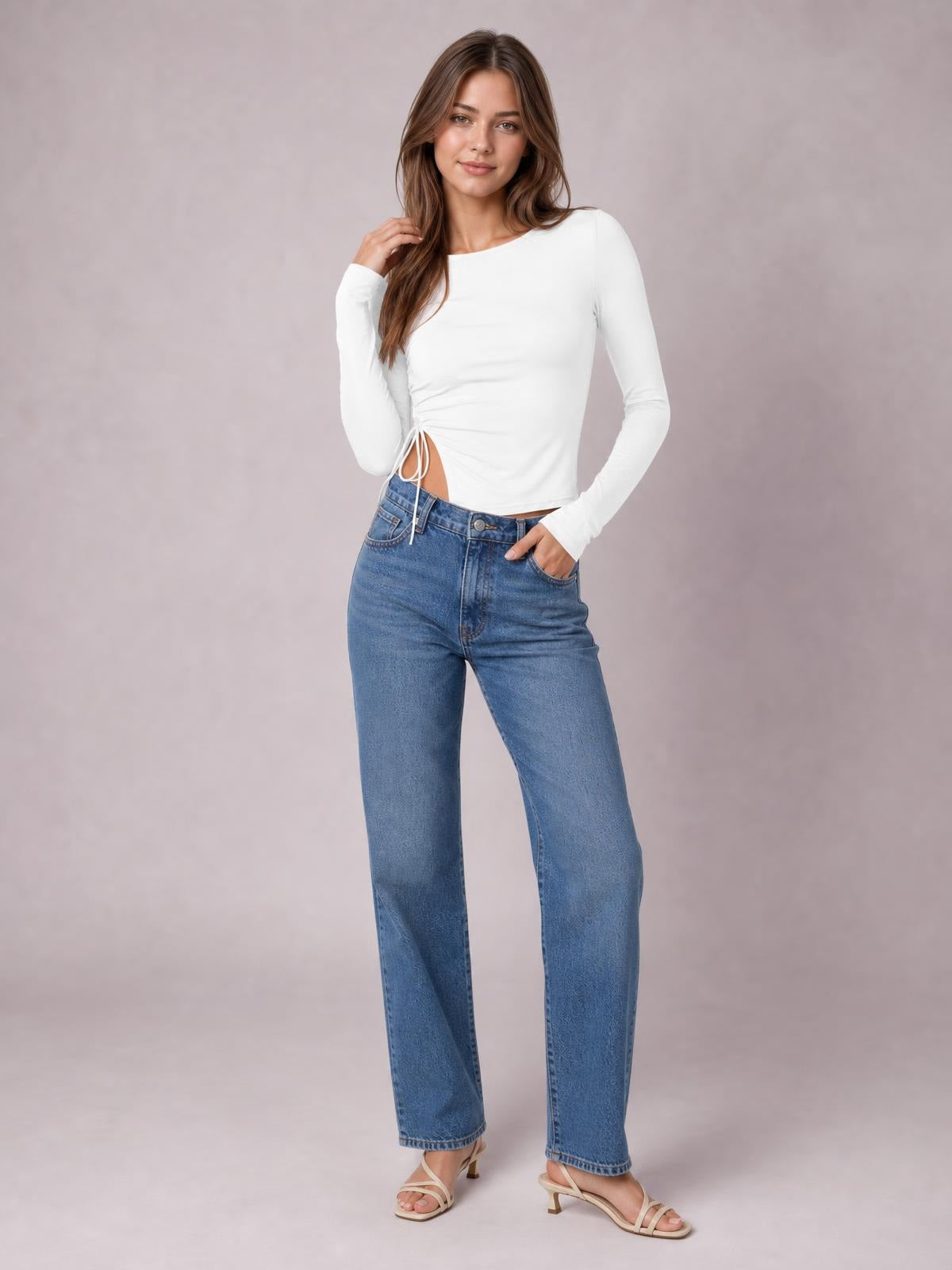 Model poses in a fitted white long-sleeve round-neck T-shirt with a tied side slit creating a cutout waist detail and modern silhouette.