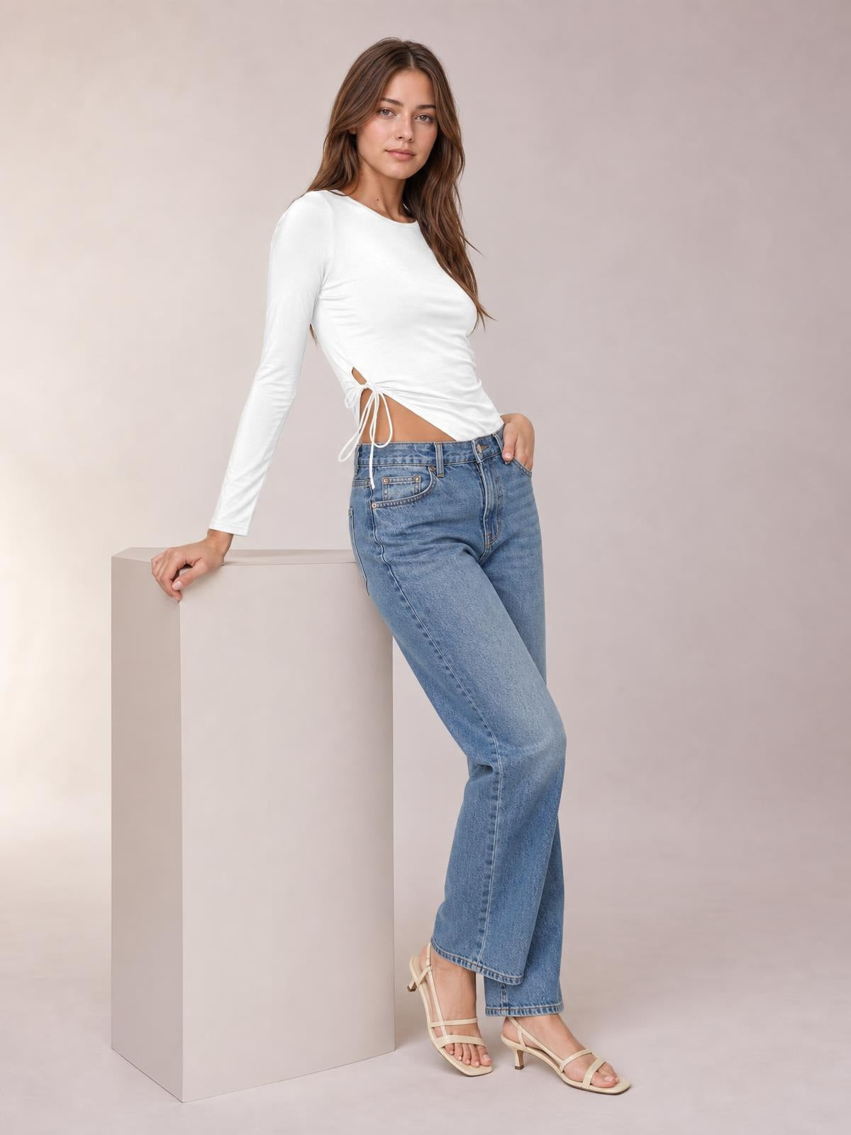 Model poses in a fitted white round-neck long-sleeve T-shirt with a tied side slit detail and slightly cropped silhouette.