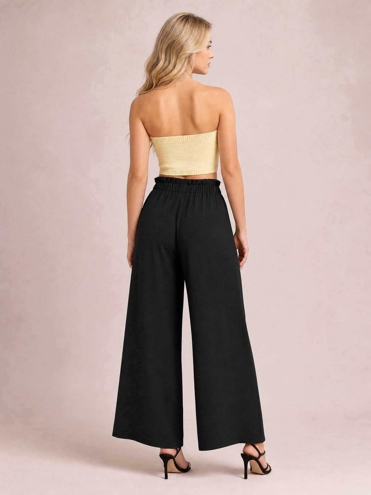 Back view of a model wearing black wide-leg pants with an elastic waist and flowing full-length silhouette, styled with a cropped strapless top.