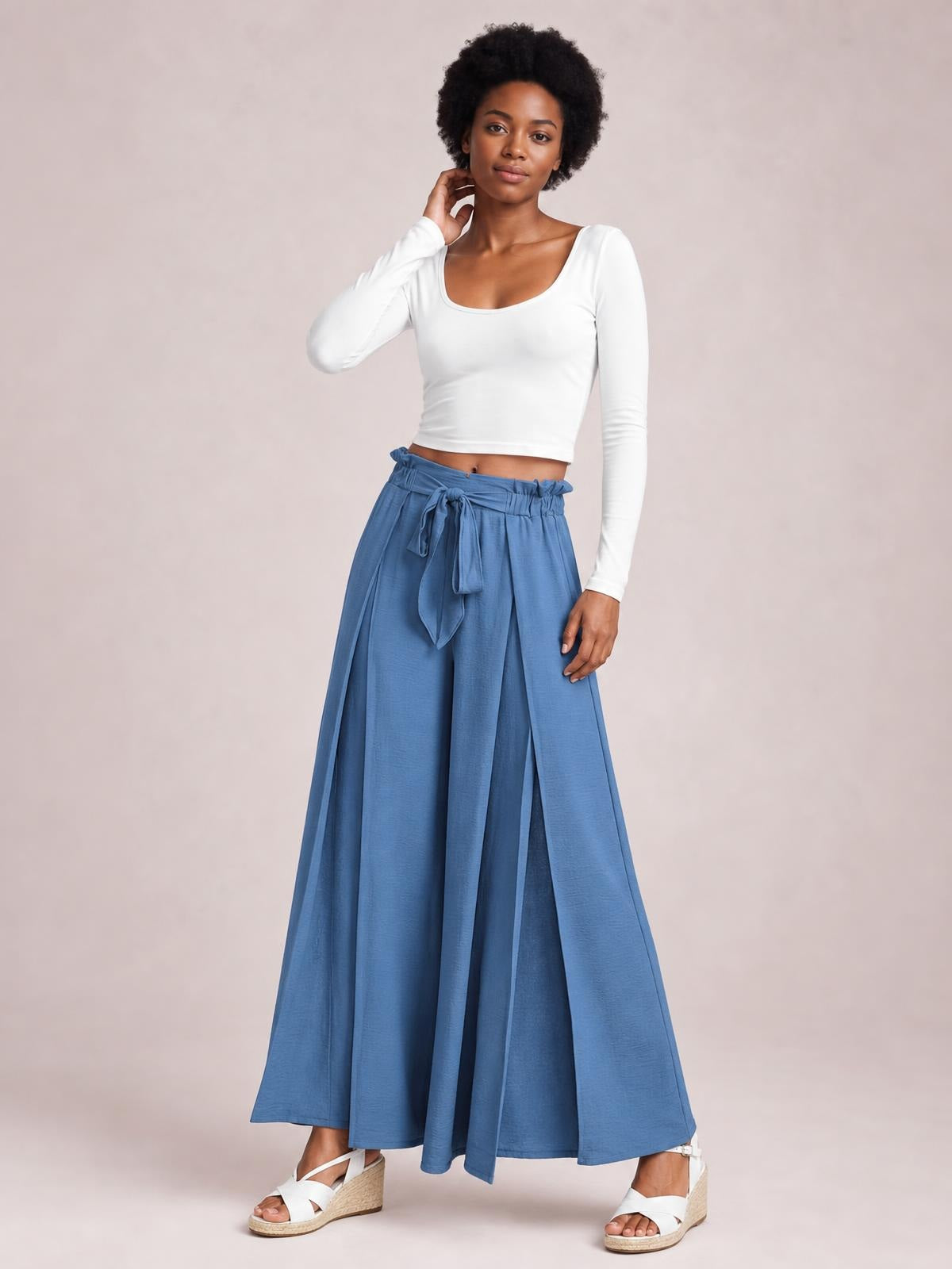 A model poses in blue tied slit wide-leg pants with a flowing, floor-length silhouette and gathered waistband.