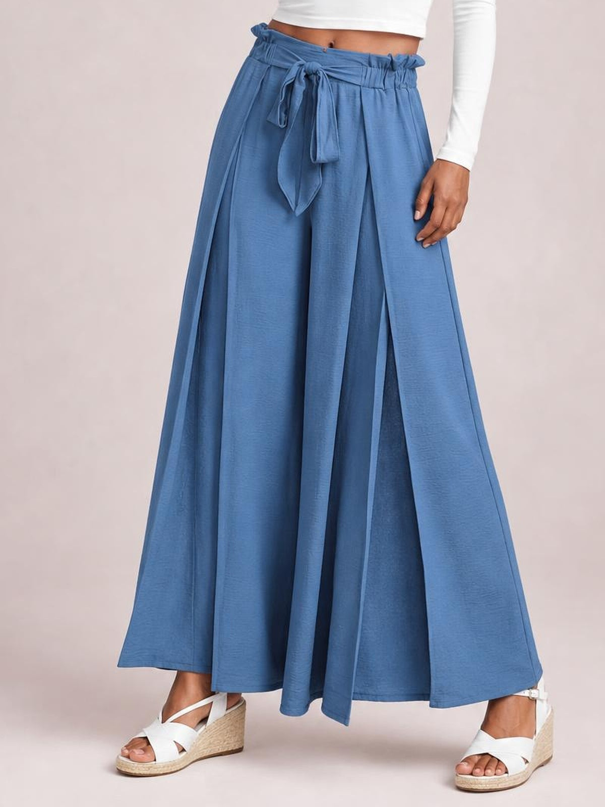 Model stands in blue tied slit wide-leg pants with a gathered elastic waist, flowing panels, and an ankle-length silhouette.