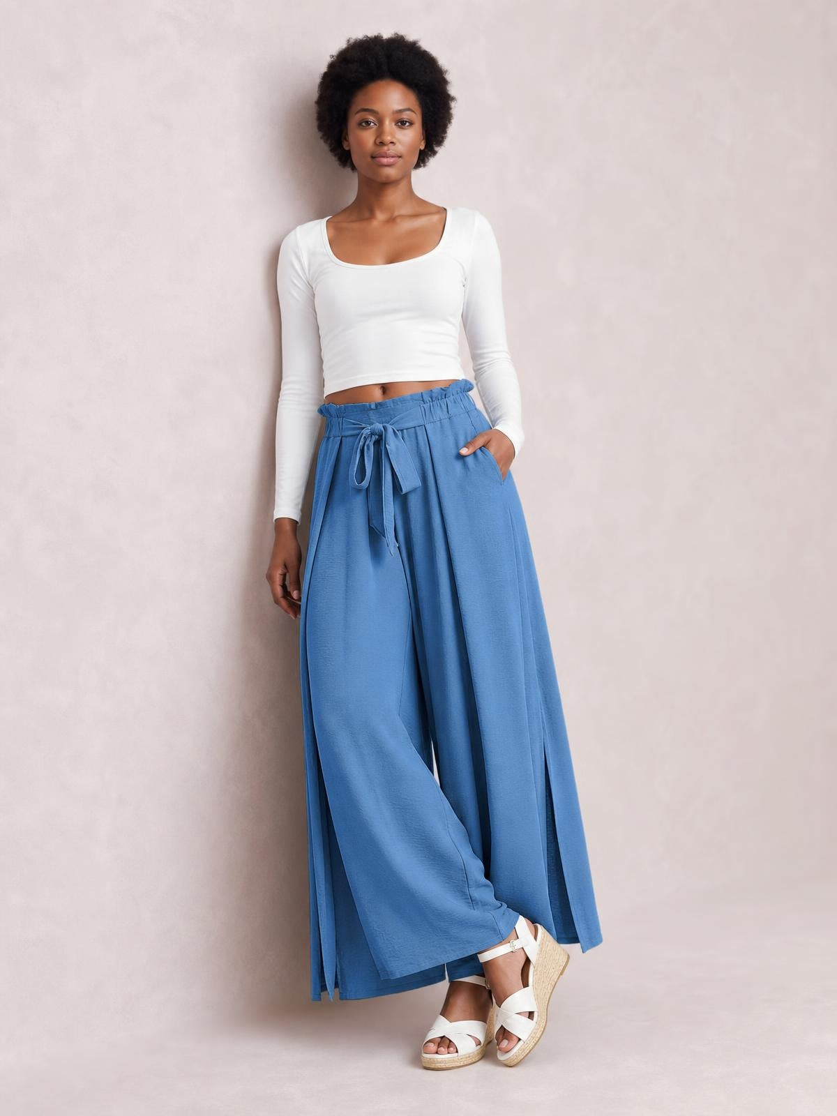 A model poses in blue tied slit wide-leg pants with a relaxed silhouette, elastic waistband, flowing construction, and one hand resting in a pocket.