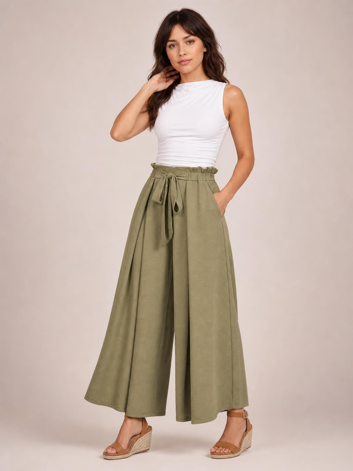 A model poses in olive tied slit wide leg pants with a gathered waist, flowing ankle-length silhouette, and one hand in a pocket.