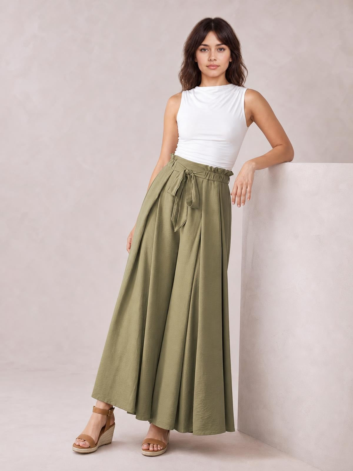 Model poses in olive-green tied slit wide leg pants with a flowing full-length silhouette, gathered waistband, and long front tie detail.