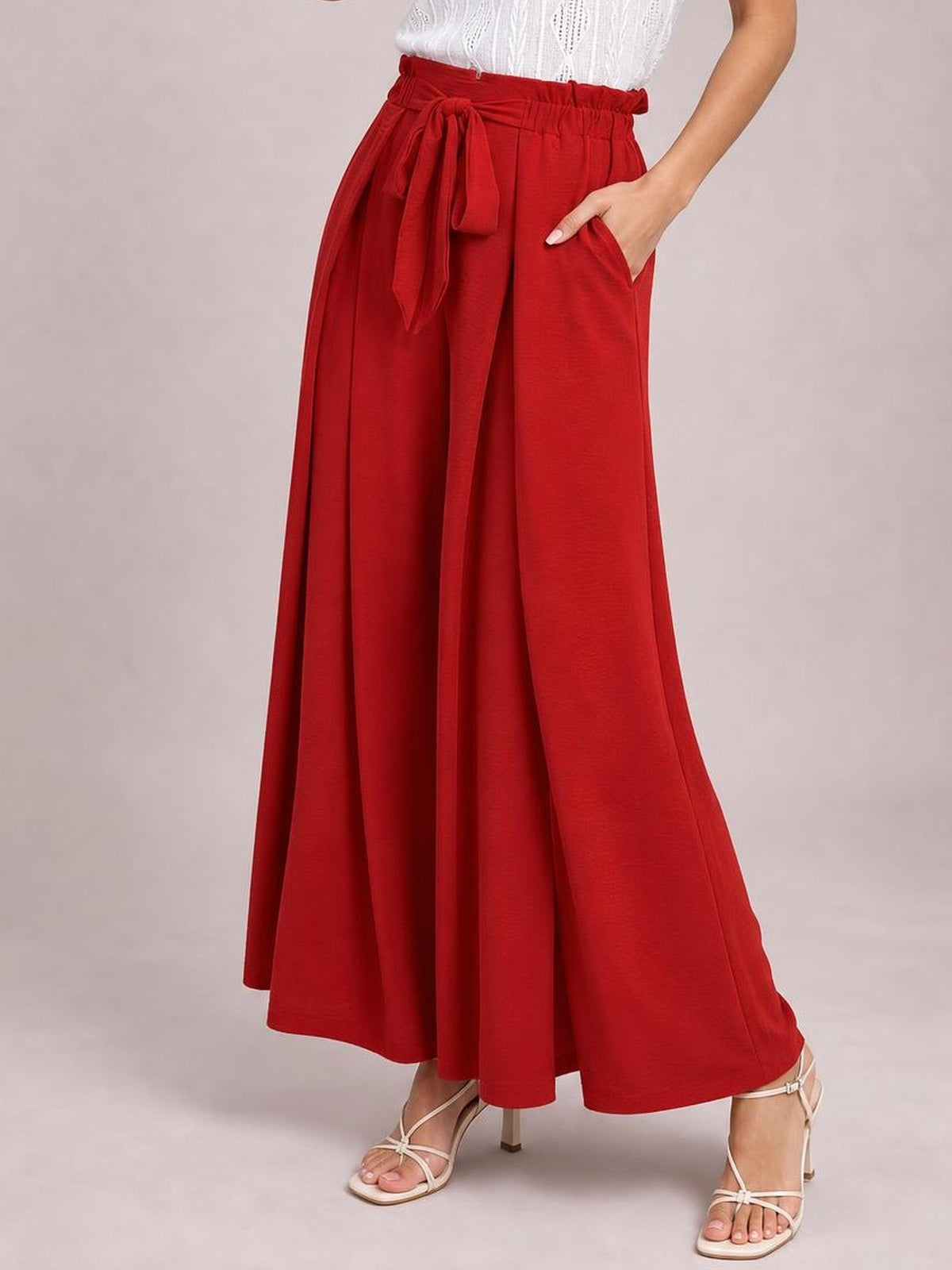 A model poses in red tied slit wide-leg pants with an elastic waist, flowing floor-length silhouette, and one hand tucked into a side pocket.
