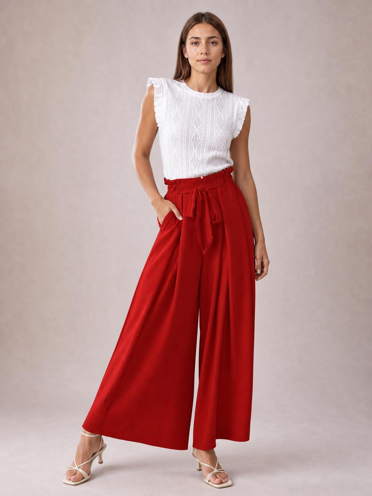 A model poses in red tied slit wide-leg pants with a high waist, flowing wide silhouette, and one hand resting in a side pocket.