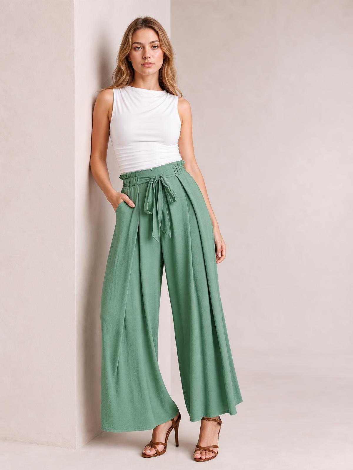 Model poses in sage green tied slit wide leg pants with a high gathered waist, flowing full-length silhouette, and side pockets.