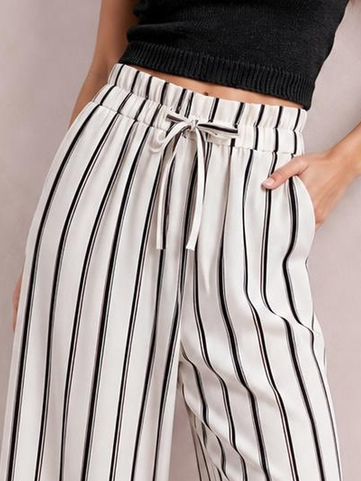 Model wears white wide-leg pants with black vertical stripes, a tied drawstring waist, and visible pockets in a relaxed pose.