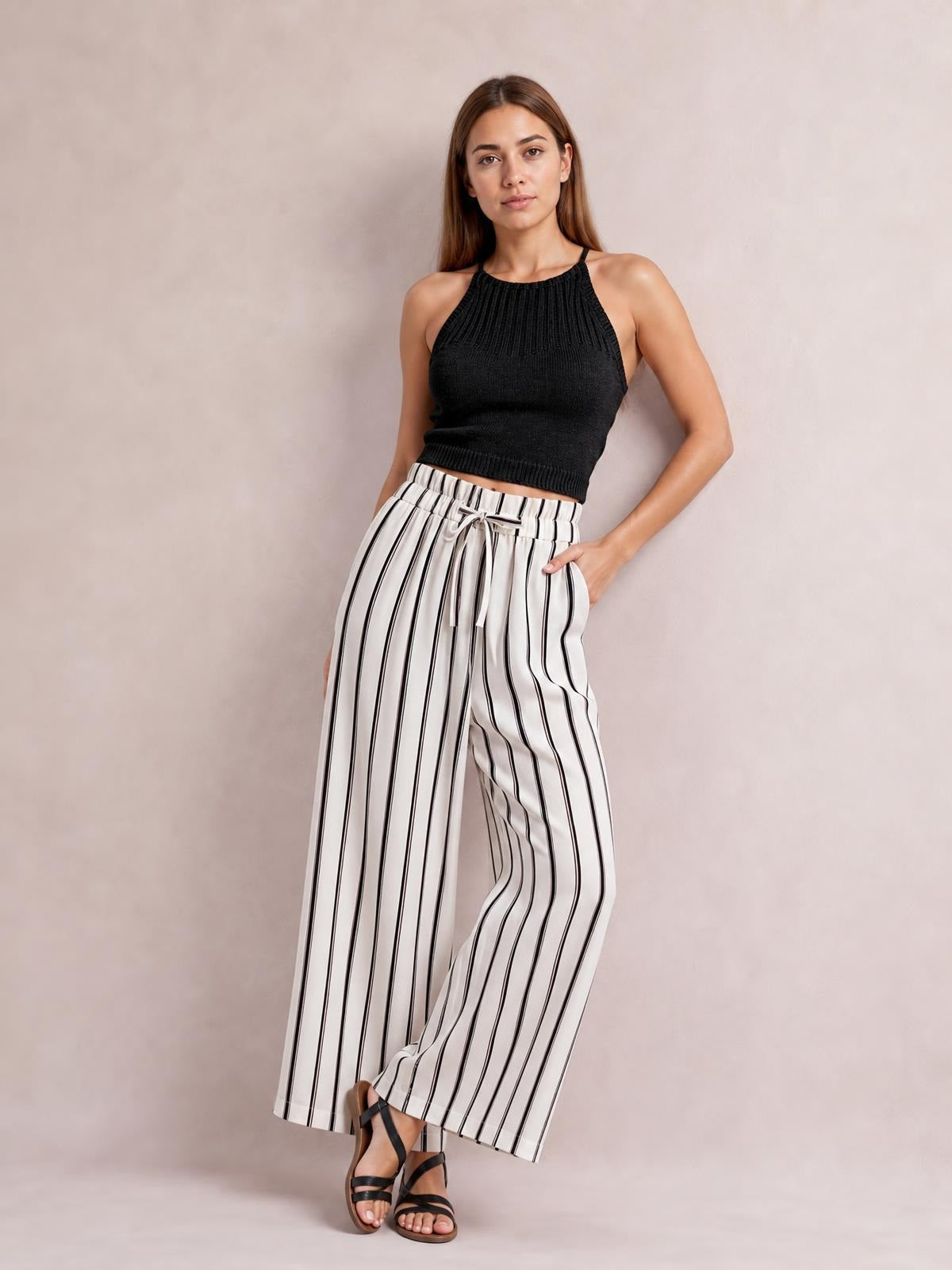 Model poses in white opaque pants with black vertical stripes, a tied drawstring waist, pockets, and a flowy wide-leg silhouette.