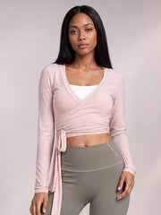 Model wears a light pink tied surplice long sleeve top with a crossover neckline, fitted cropped silhouette, and long waist tie.