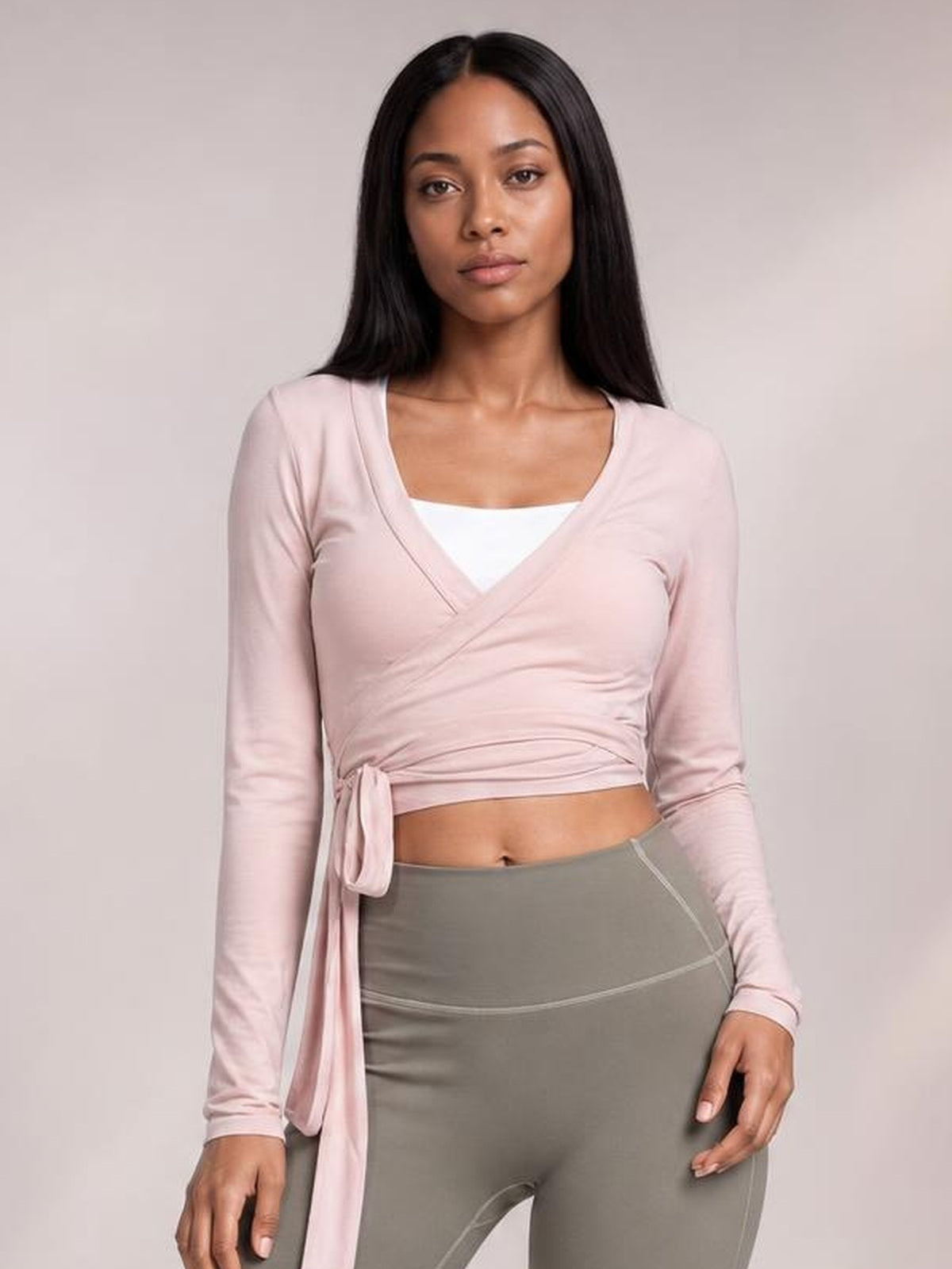 Model wears a light pink tied surplice long sleeve top with a crossover neckline, fitted cropped silhouette, and long waist tie.