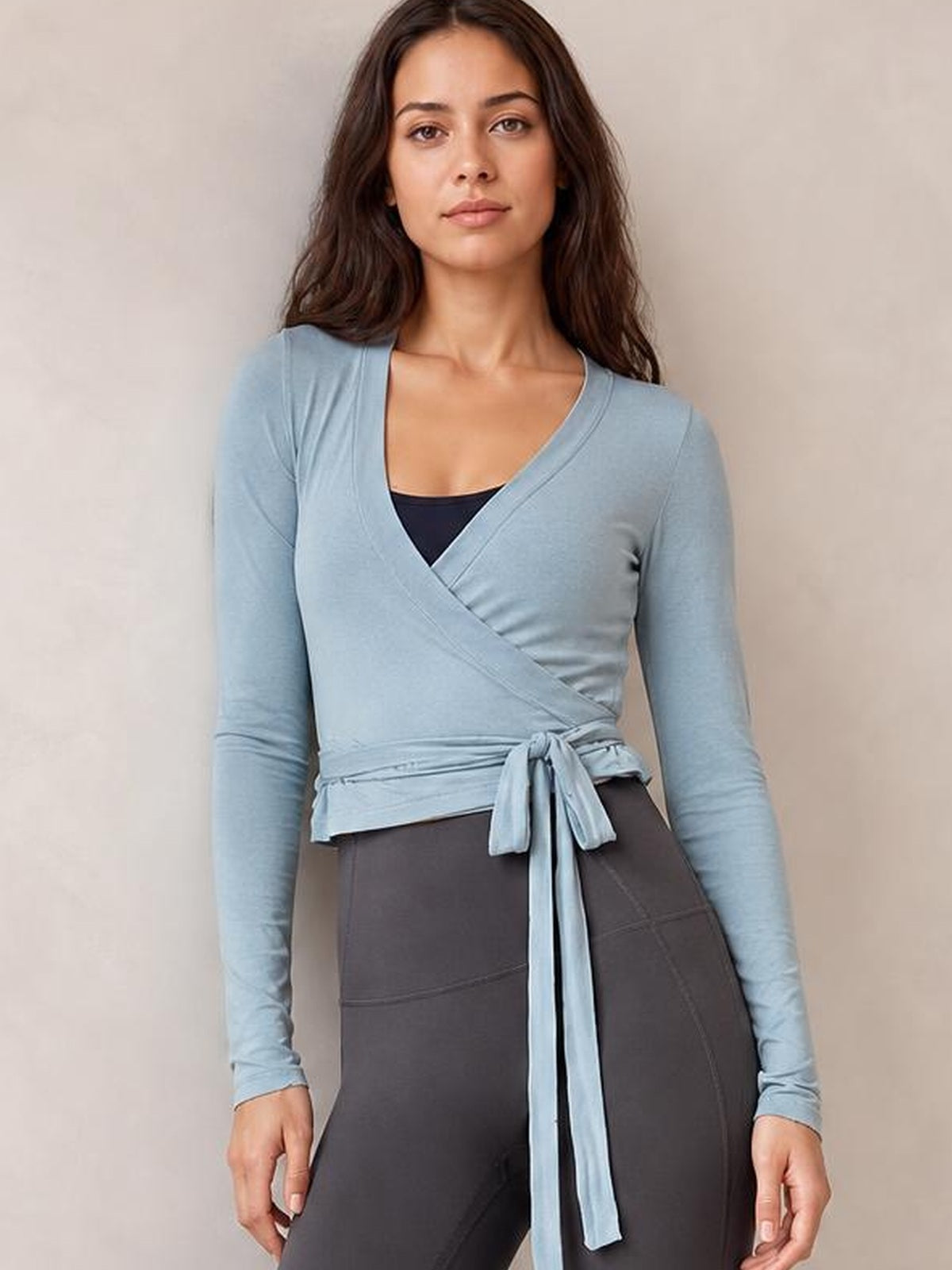 Model wearing a light blue tied surplice long sleeve top with a wrap-front silhouette, overlapping neckline, and waist sash knot.