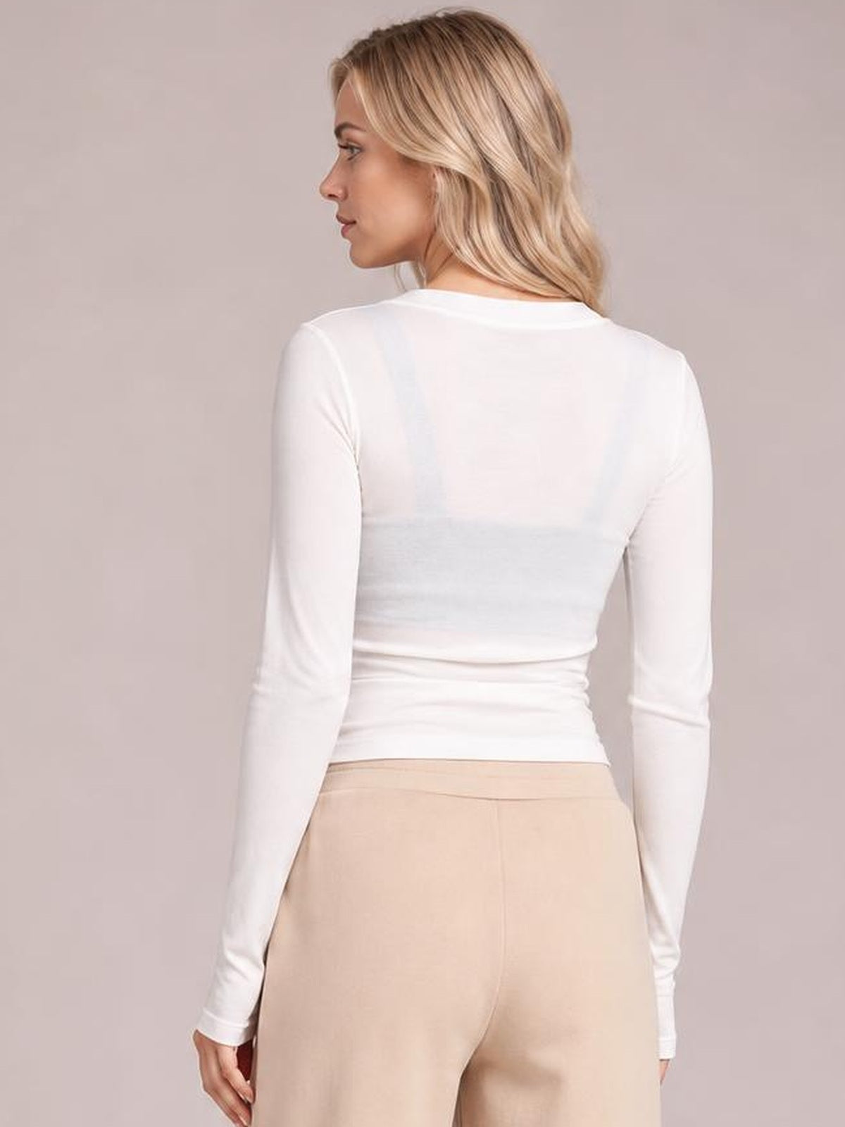 A model poses turned slightly away in a fitted white long sleeve top with a smooth crew neckline and gathered waist creating a sleek silhouette.