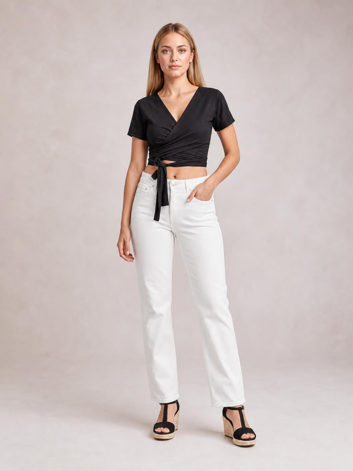 Model poses in a black tied surplice short sleeve top with a wrap-style neckline, cropped silhouette, and waist sash.