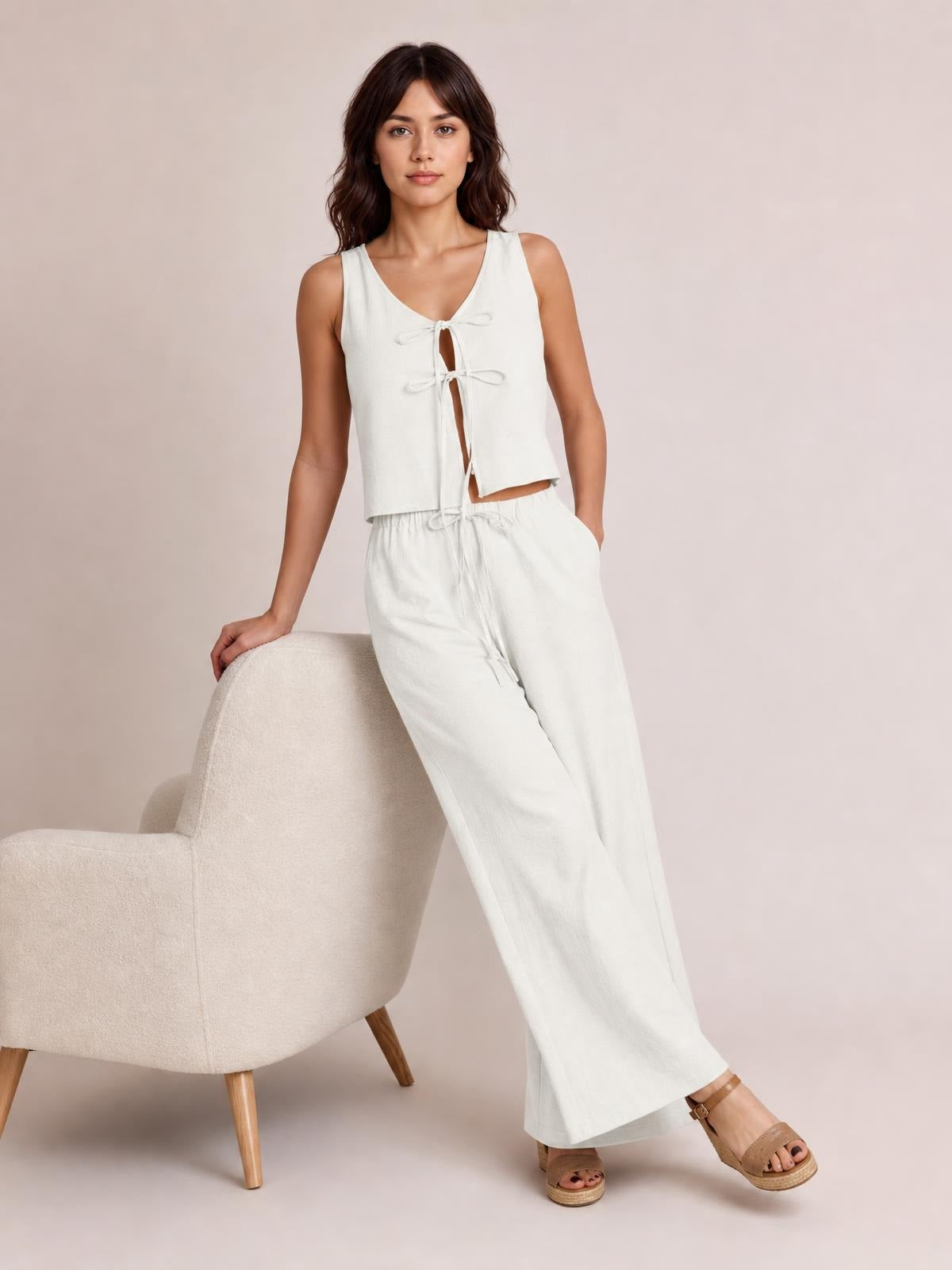 Model poses in a white sleeveless V-neck top with tied front details and matching wide-leg drawstring pants with pockets.