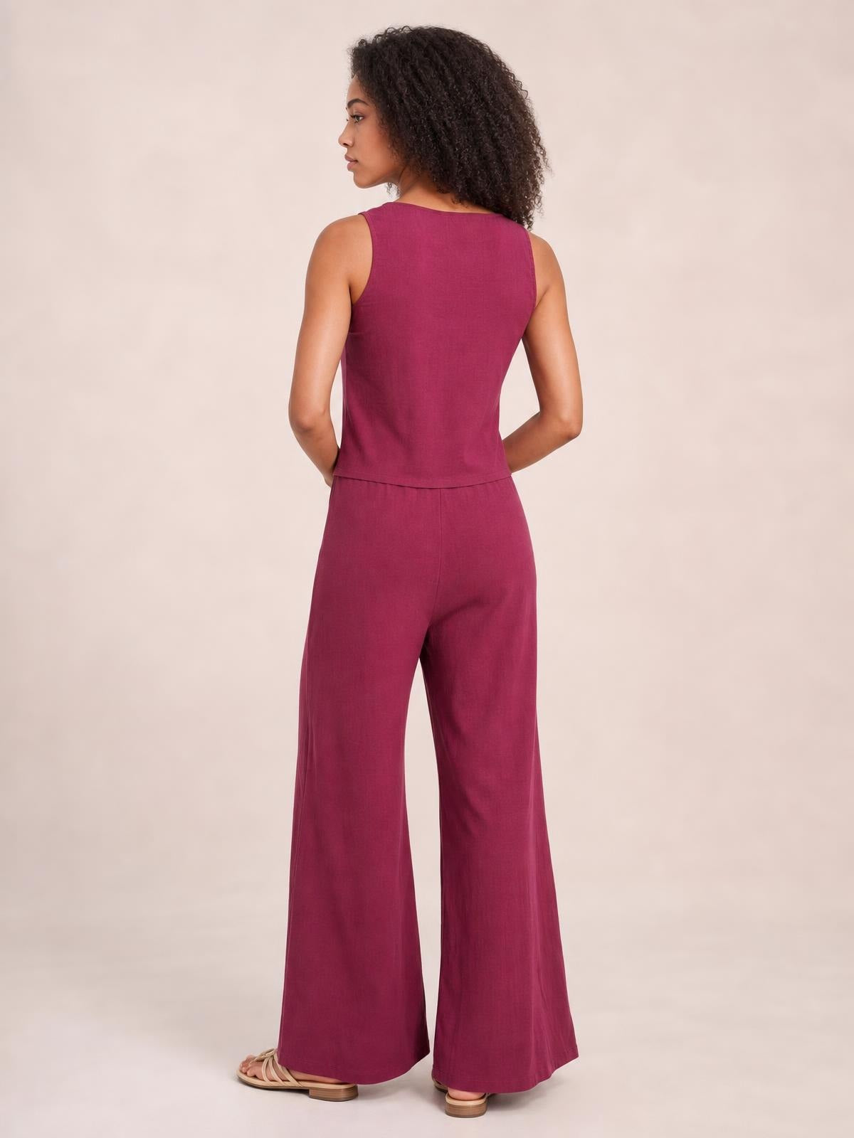 A model poses in a burgundy sleeveless top with a cropped hem and matching wide-leg pants, shown from the back with hands resting at her waist.