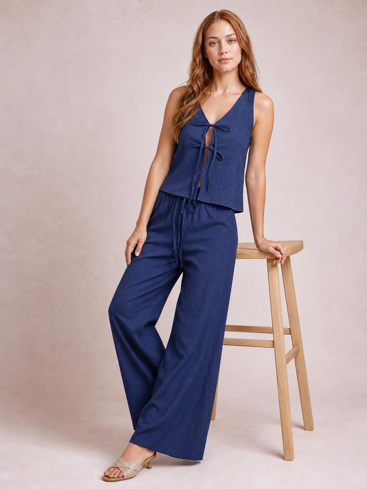 Model poses beside a stool in a navy sleeveless V-neck top with tied front and matching drawstring wide-leg pants for a relaxed, coordinated silhouette.