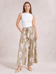 Model poses with one hand in her pocket wearing beige floral wide-leg pants with a tied waist and flowing slit-leg construction.
