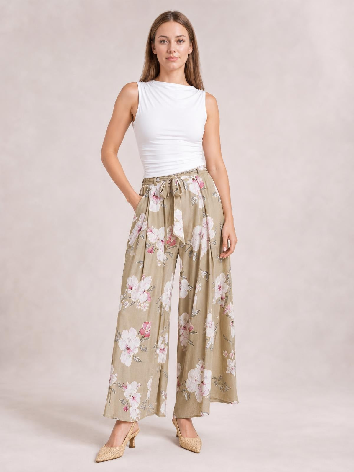 Model poses with one hand in her pocket wearing beige floral wide-leg pants with a tied waist and flowing slit-leg construction.