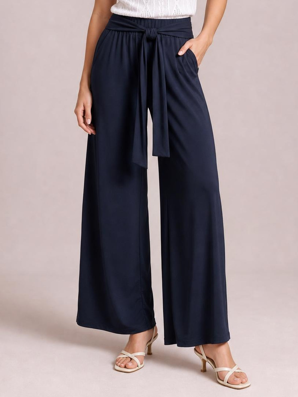 Model wears navy tied wide-leg pants with an elastic waist, long flowing silhouette, front tie, and side pockets, posing with one hand tucked in a pocket.