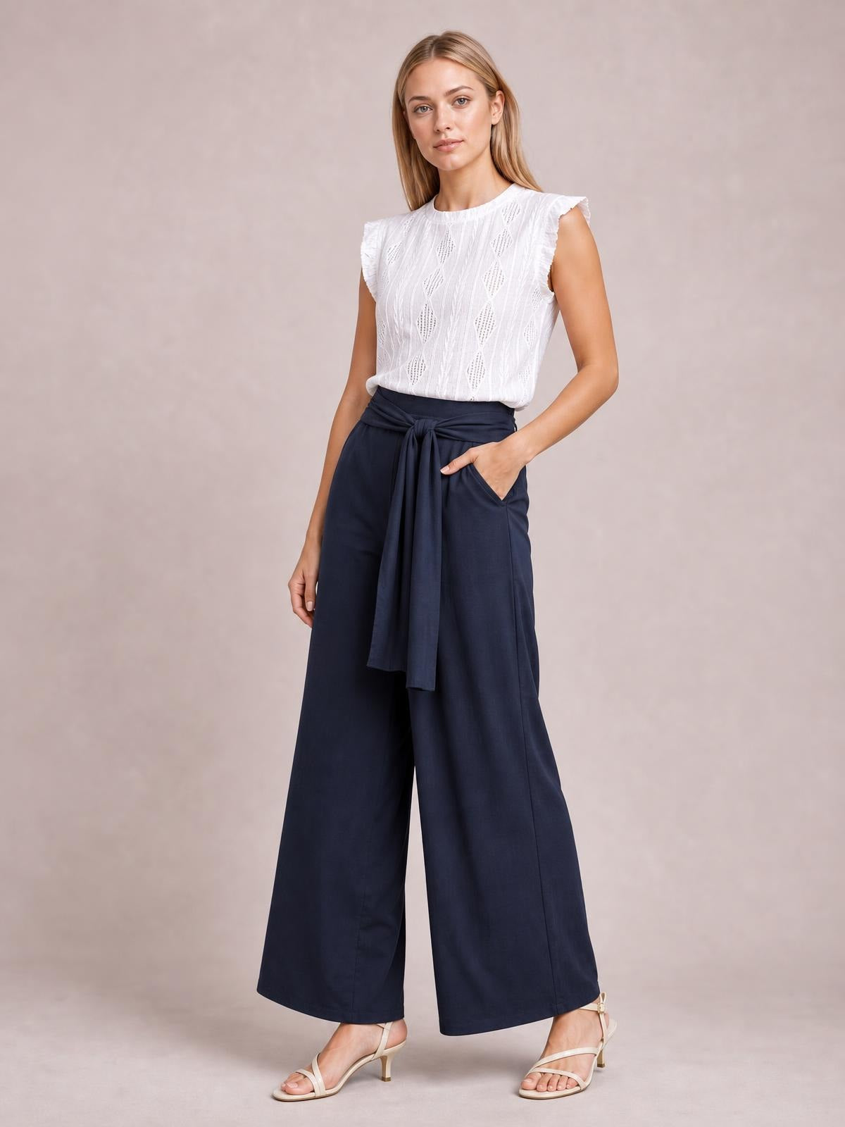 Model wearing navy tied wide-leg pants with a high waist, long flowing silhouette, and side pockets, posing with one hand tucked into a pocket.