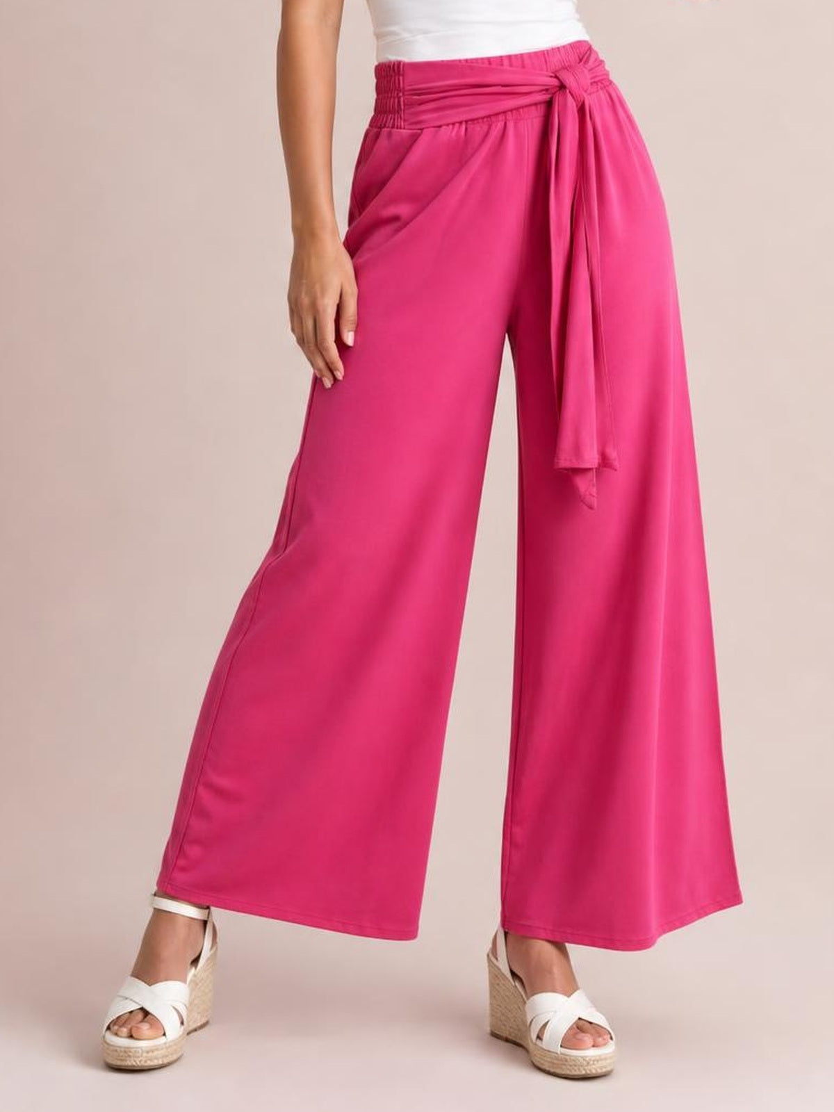 A model stands in bright pink tied wide-leg pants with a high gathered waist, flowing silhouette, side pockets, and a long front tie.