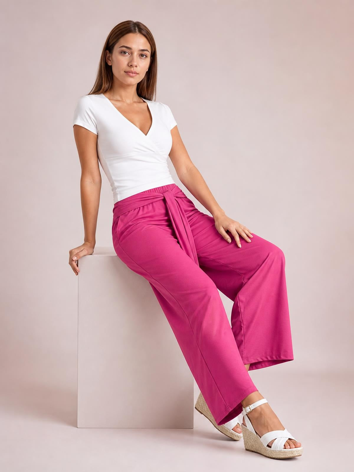 A seated model wears bright pink tied wide leg pants with a relaxed silhouette, wide hems, and visible side pockets.