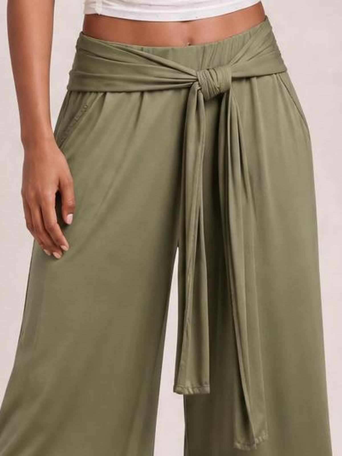 Model wears olive green tied wide leg pants with a wrap-style waist, long hanging tie ends, relaxed silhouette, and visible side pockets.
