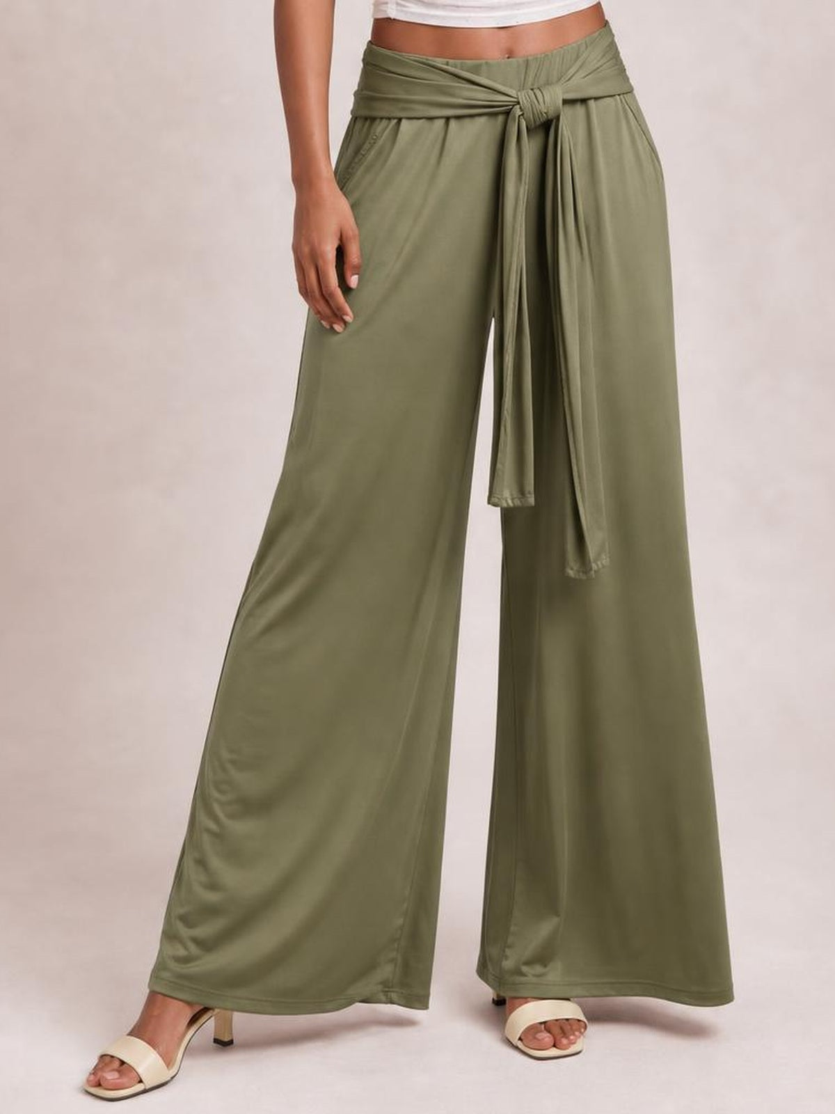 Model wearing olive green tied wide leg pants with side pockets, a draped waist sash, and a flowing full-length silhouette.