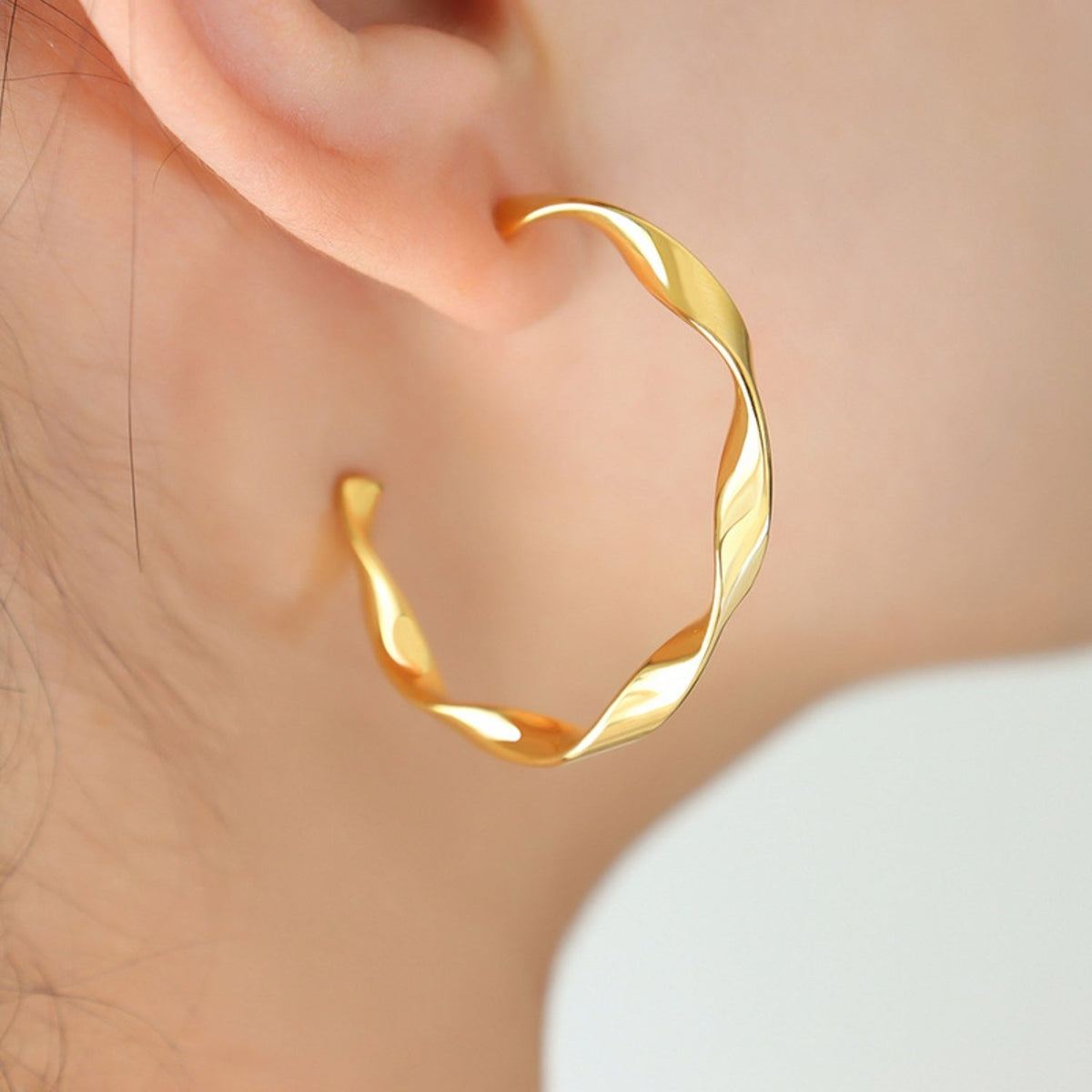 Close-up of a gold-tone titanium steel C-hoop earring on an ear, featuring a sleek curved silhouette and subtly twisted polished construction.