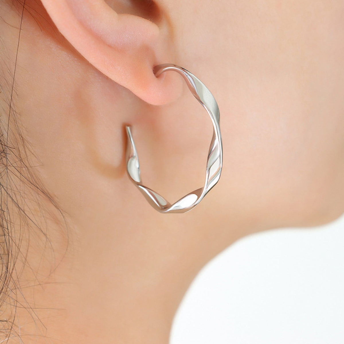 Close-up of a visible ear wearing a polished silver-tone titanium steel C-hoop earring with a smooth, sculptural curved silhouette and textured twists.