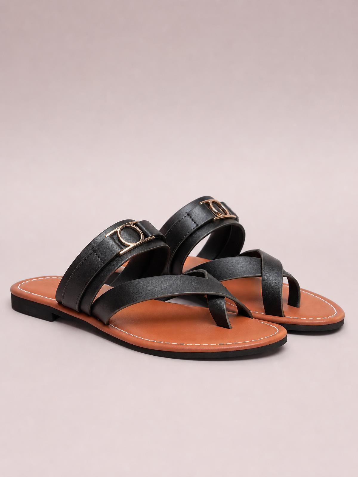 Black toe loop flat sandals with wide crisscross straps, gold-tone accents, brown footbeds, stitched edges, and low black soles.