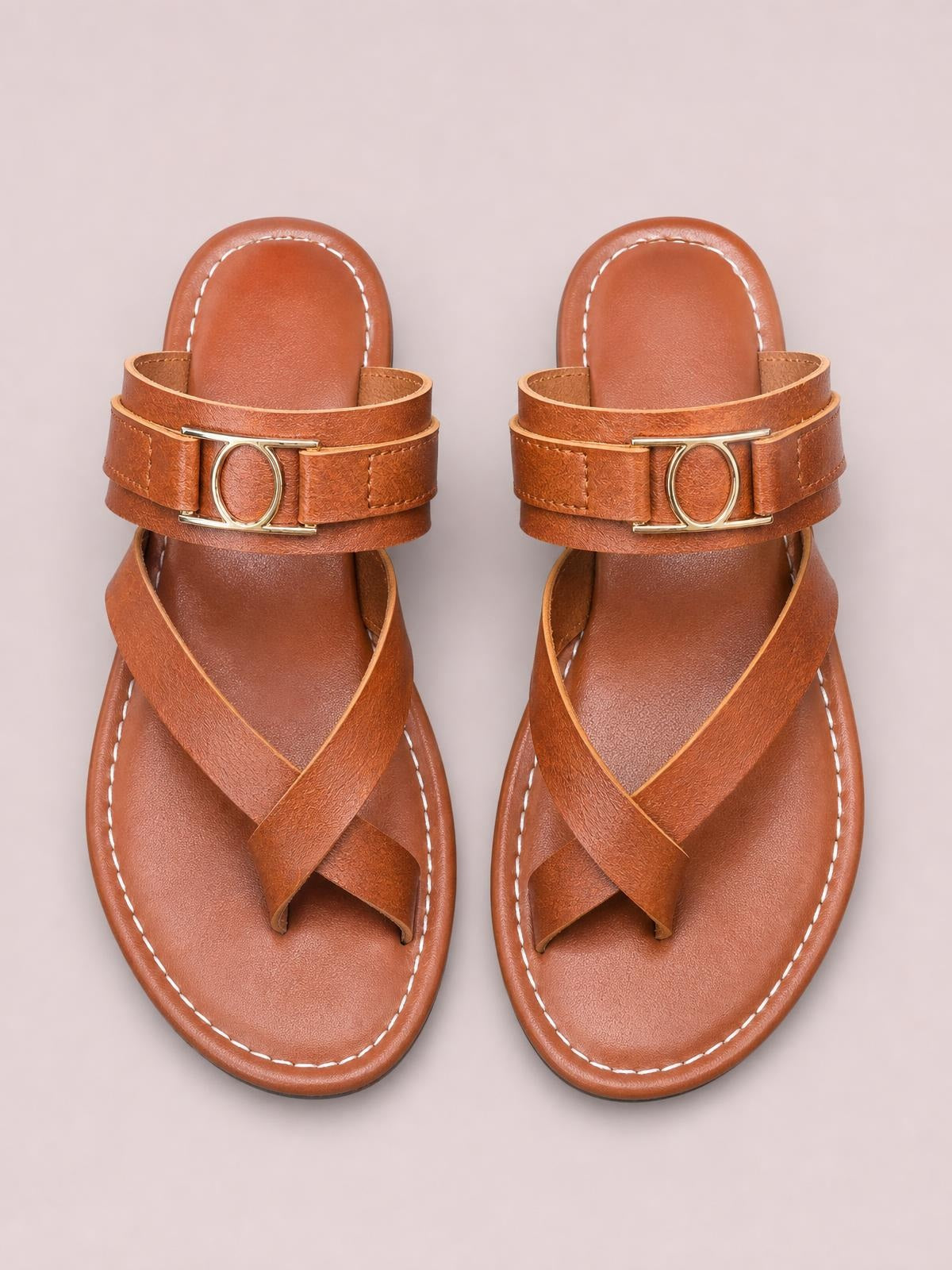 Cognac-brown toe loop flat sandals with crossed open-toe straps, stitched edges, and oval metal accents on the uppers.