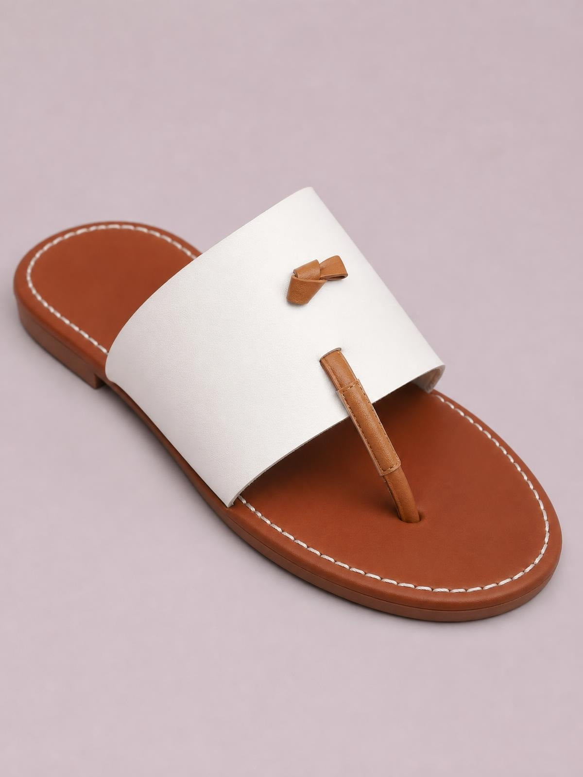 White and brown toe post flat sandals with a wide upper strap, brown footbed, decorative bow, and stitched rubber sole.