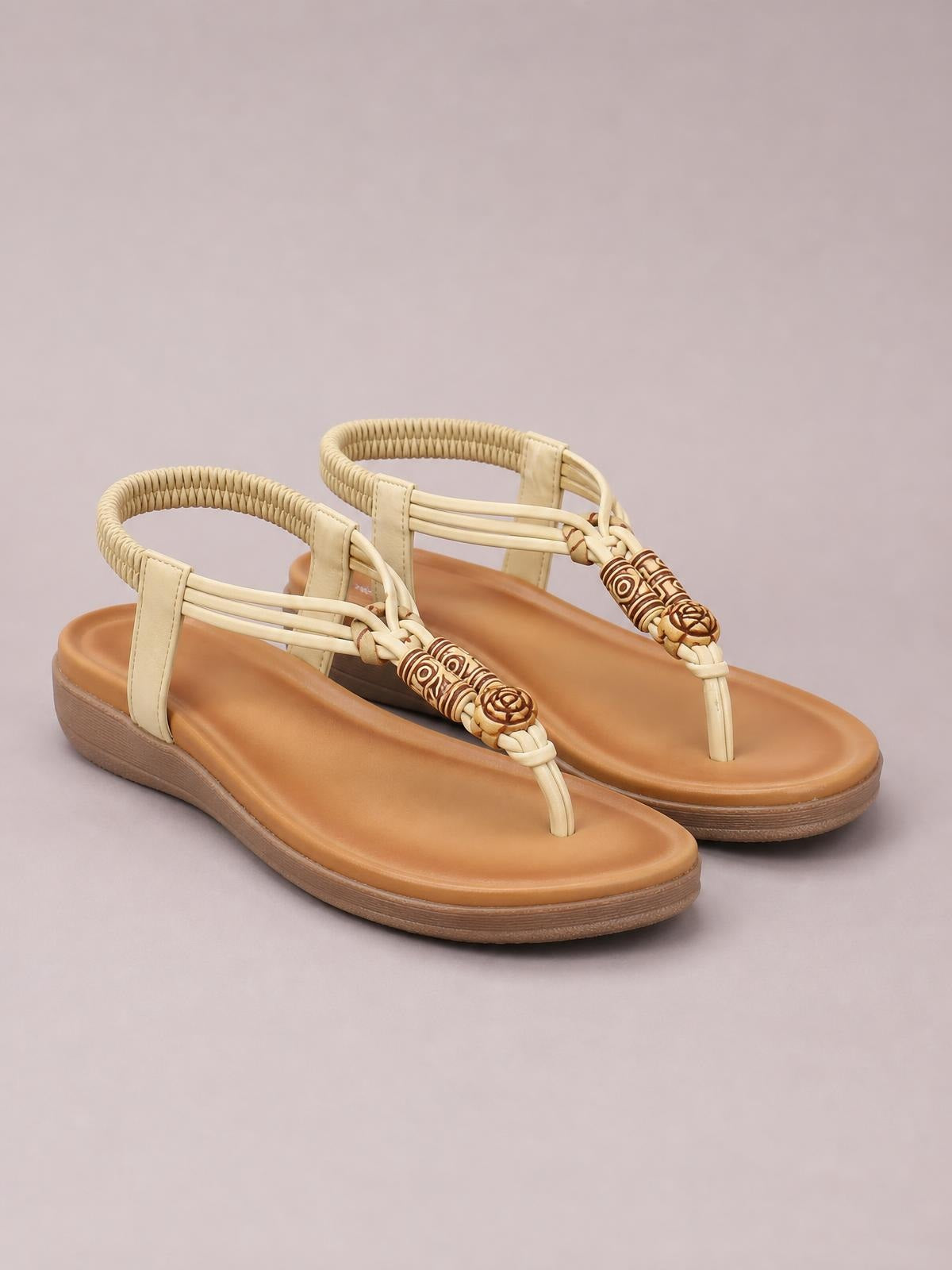 Beige toe post flat sandals feature woven ankle straps, decorative braided detailing, tan footbeds, and low rubber soles.
