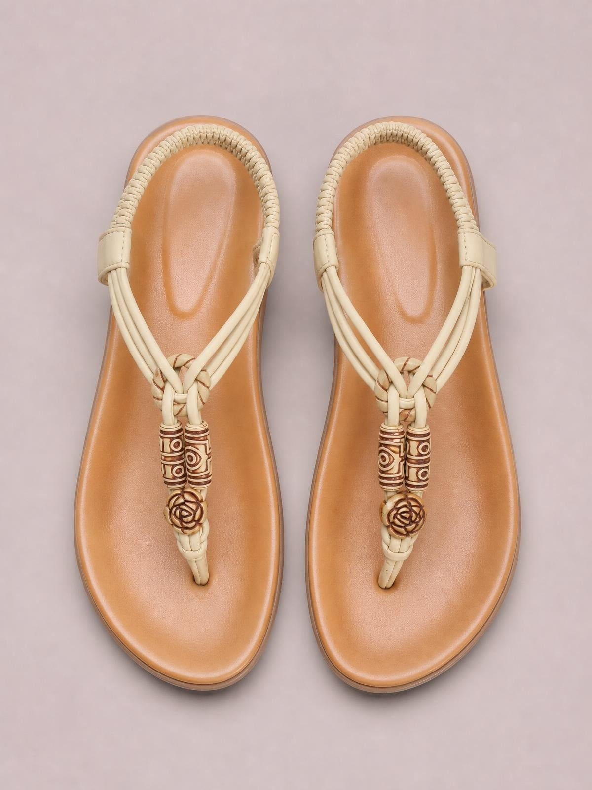 Cream toe post flat sandals feature braided straps, tan footbeds, rounded toes, and decorative patterned bead and floral accents.