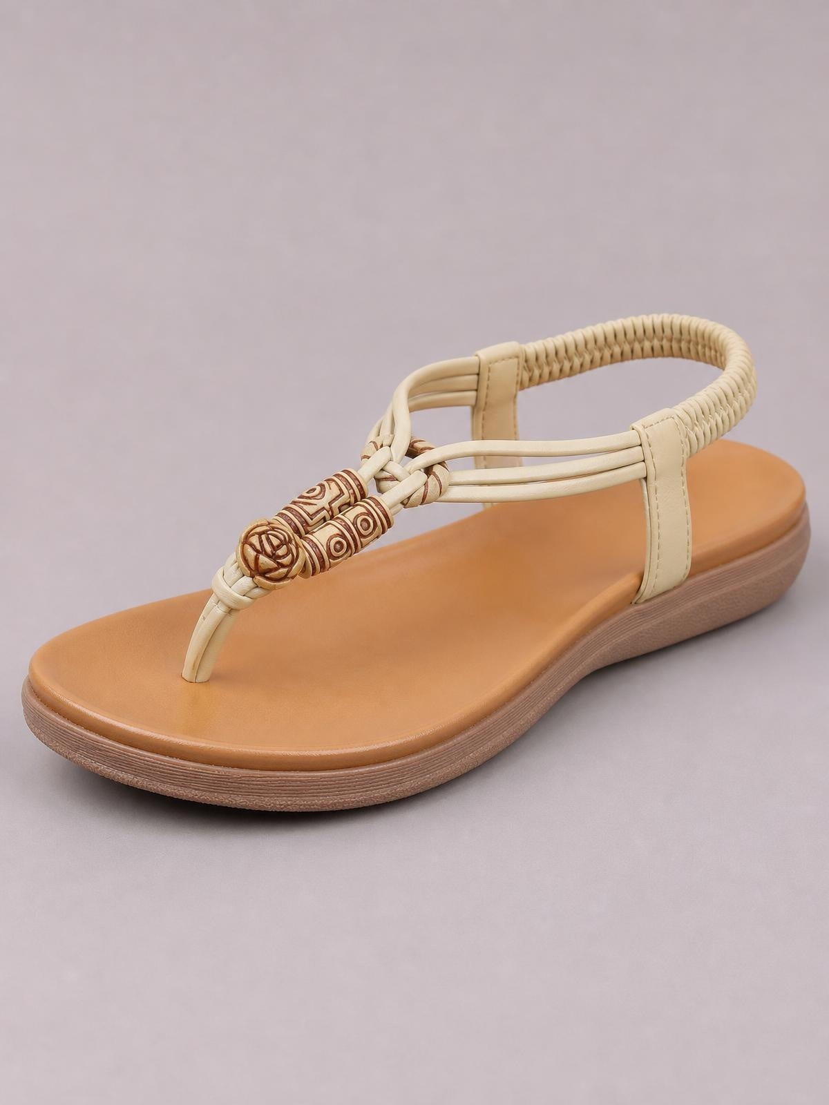 Tan toe post flat sandal with cream braided straps, decorative beaded accents, cushioned footbed, and a textured rubber sole.