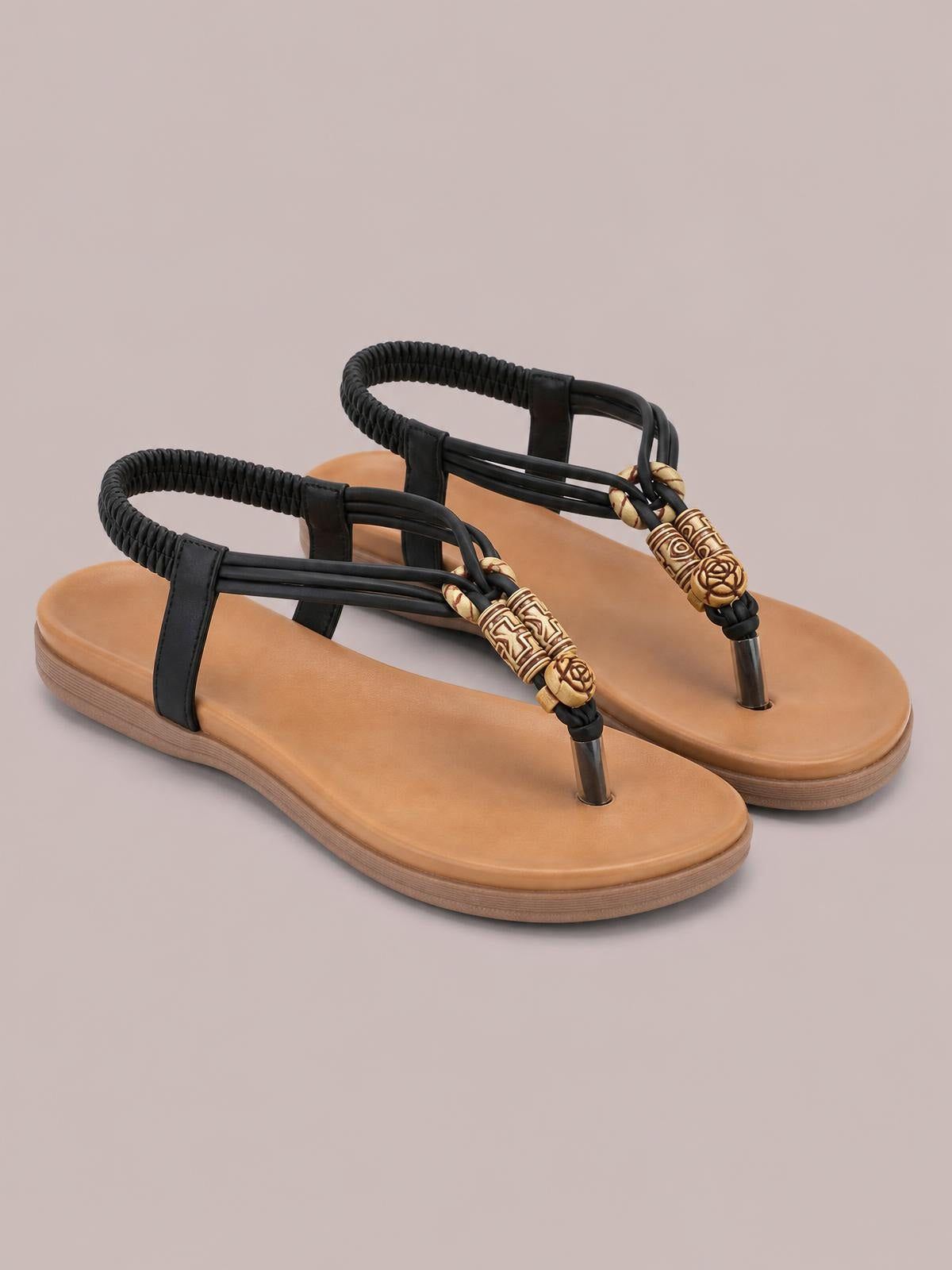 Black toe post flat sandals feature tan footbeds, braided ankle straps, decorative carved beads, and low rubber soles in a strappy design.