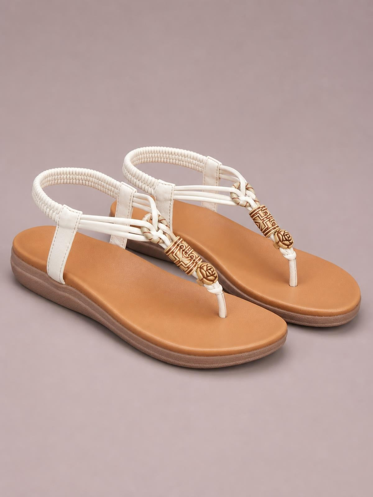 White toe post flat sandals with tan footbeds, woven ankle straps, decorative gold-tone accents, and low rubber soles.