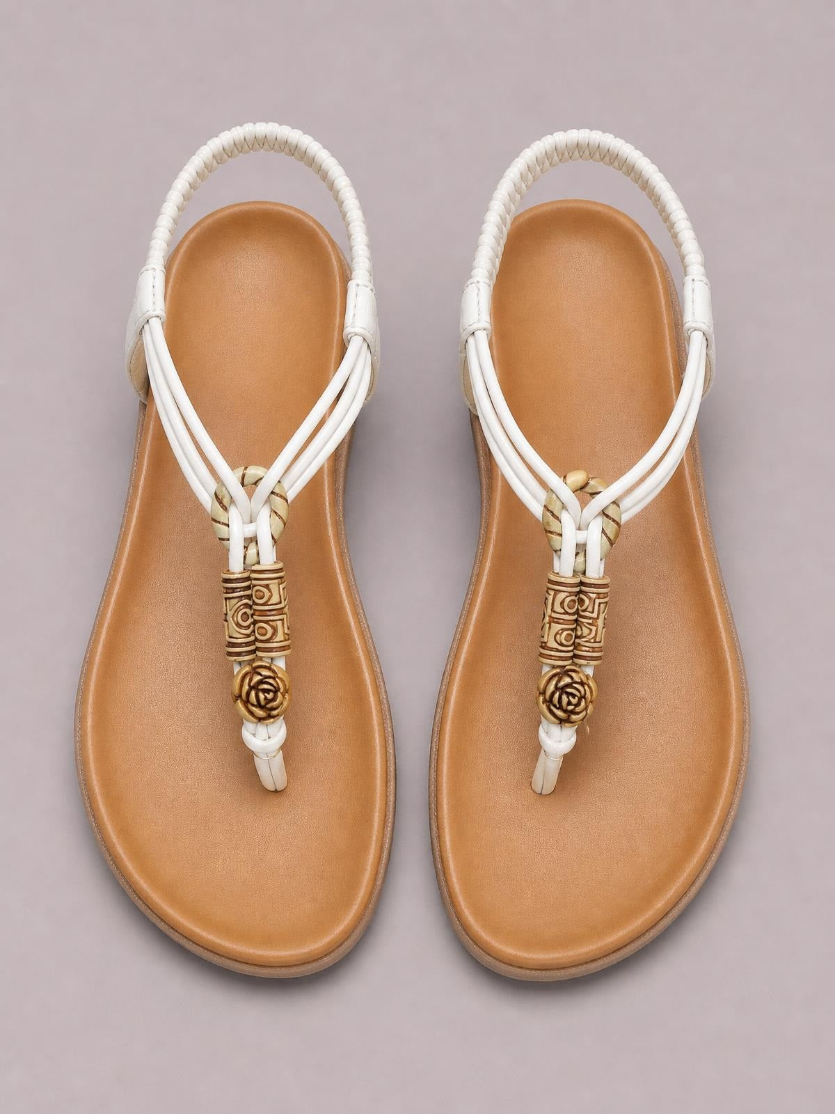 Tan toe post flat sandals with white strappy uppers, decorative beaded accents, cushioned footbeds, and slim rubber soles.