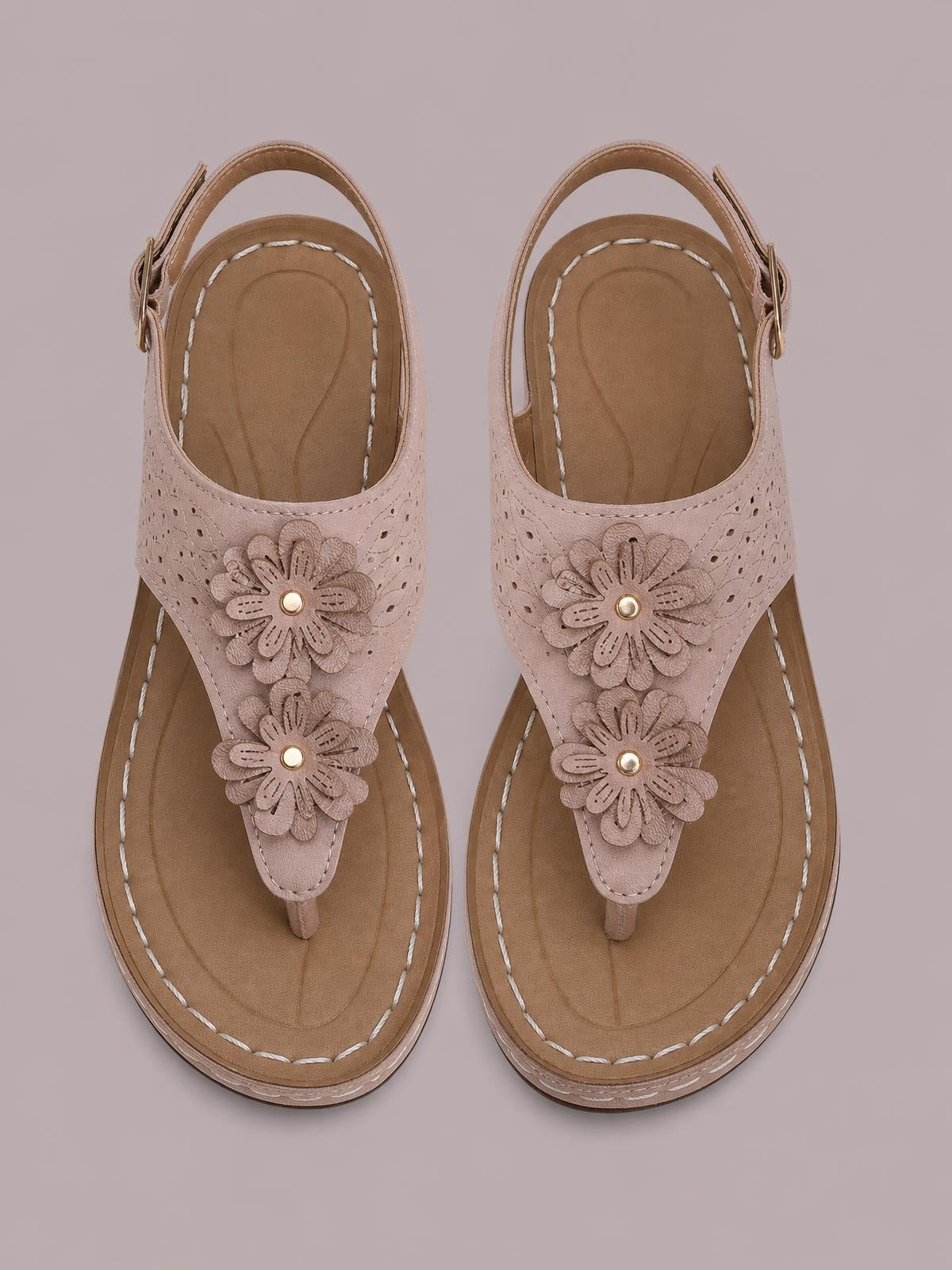 Blush pink toe post wedge sandals feature layered flower details, perforated uppers, ankle straps, stitched footbeds, and comfortable mid-height heels.