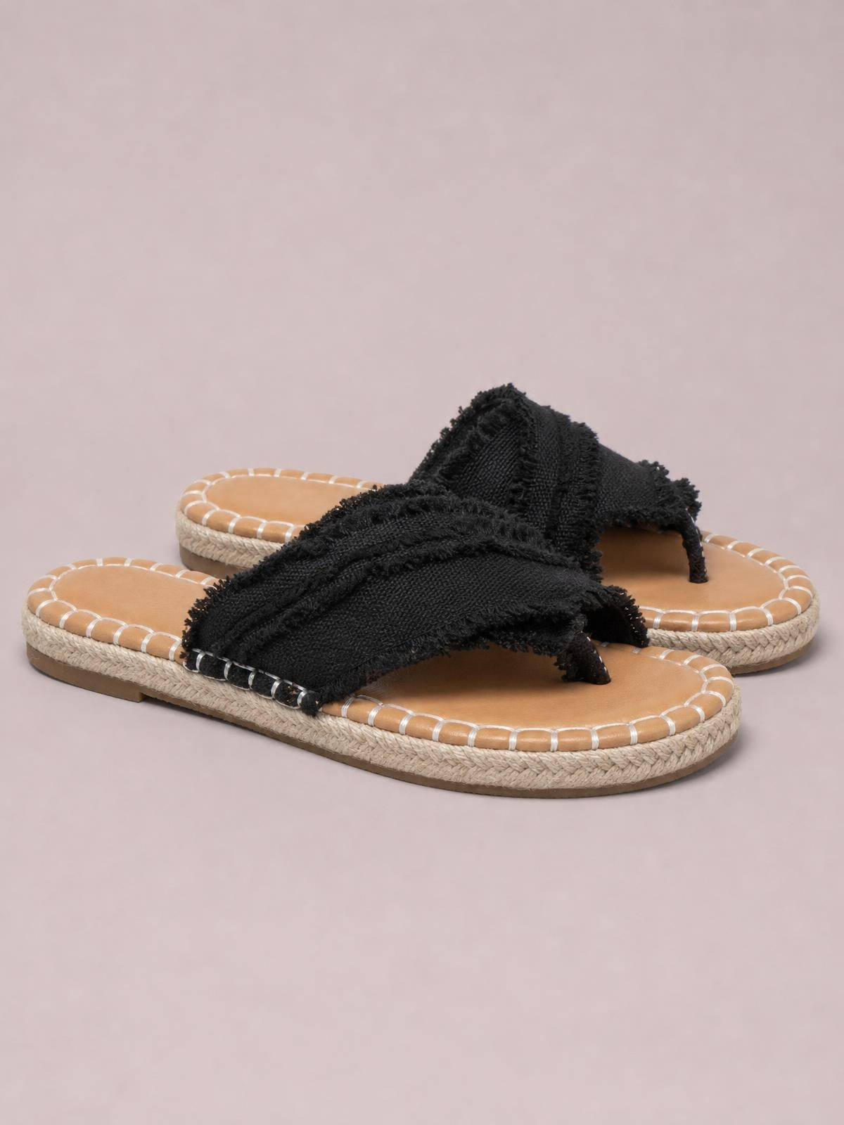 Black canvas toe post flat sandals feature raw frayed edges, wide crossover straps, tan footbeds, and textured woven midsoles over rubber soles.