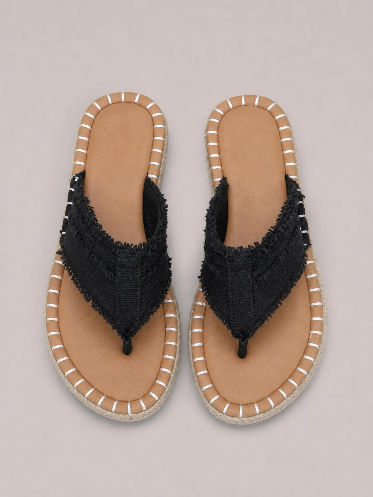 Black canvas toe-post flat sandals feature frayed raw-edge straps, tan footbeds, white striped trim, and rope-textured soles.