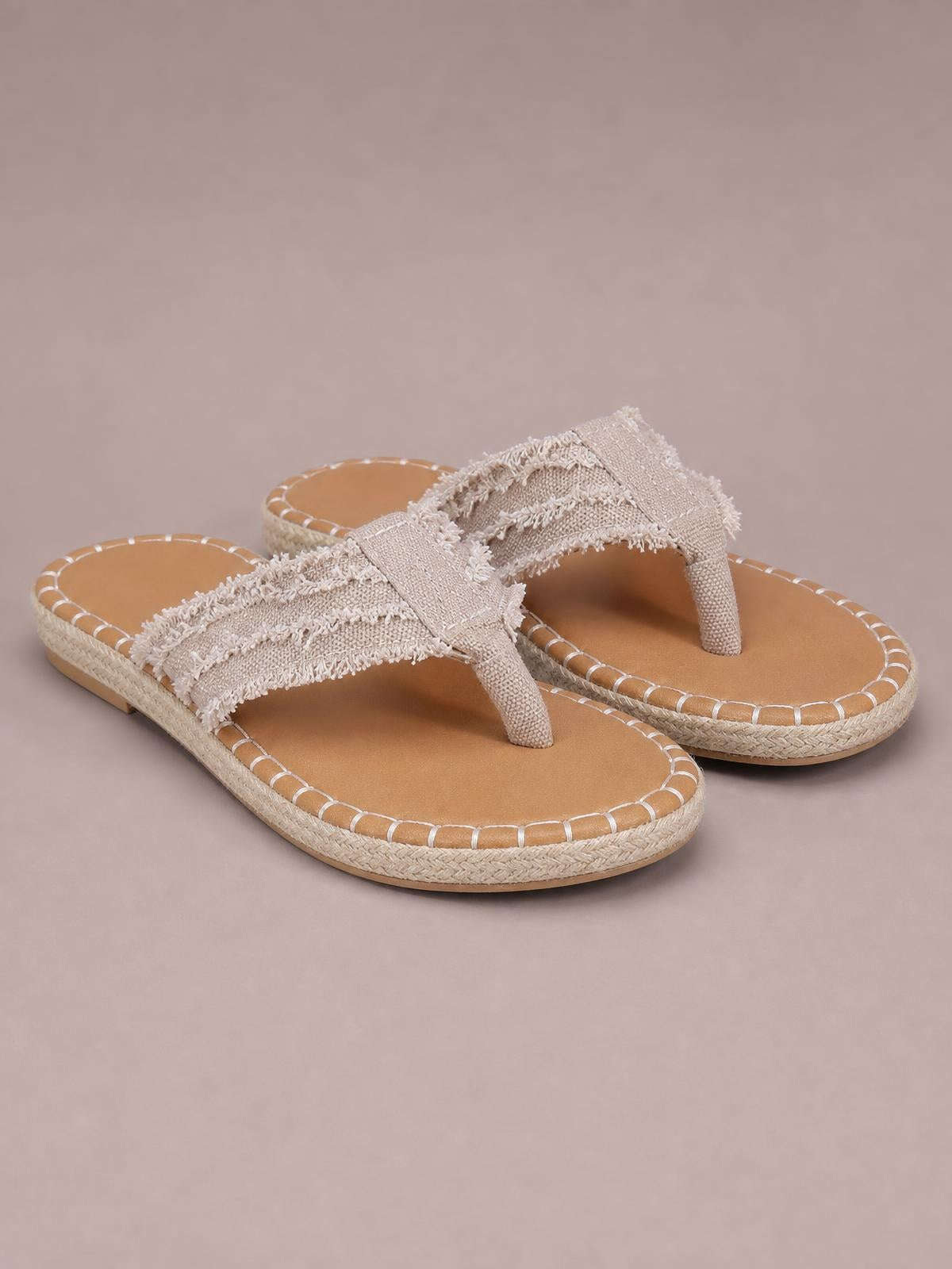 Beige canvas toe post flat sandals feature fringed raw hems, cross straps, tan footbeds, and textured rubber soles with stitched edging.