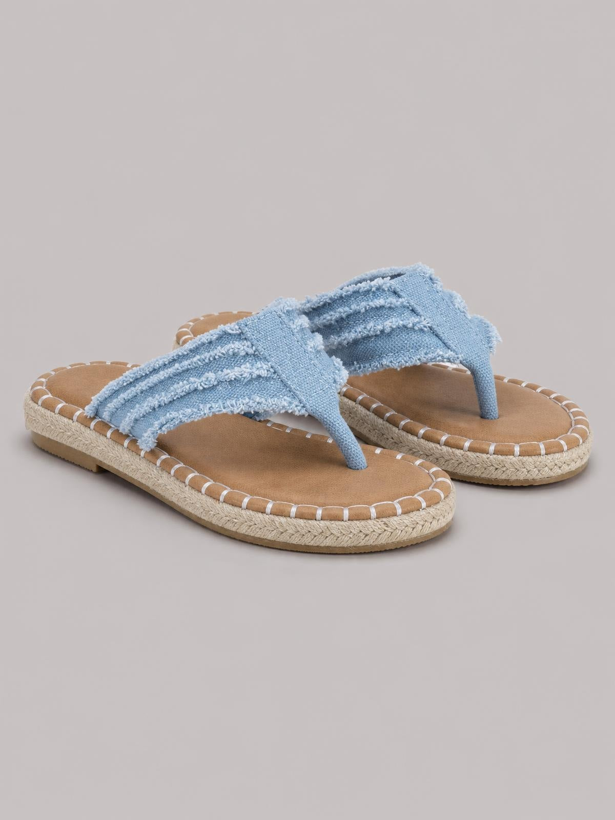 Light blue canvas toe post flat sandals feature raw-frayed straps, tan footbeds, and textured woven soles with stitched edging.