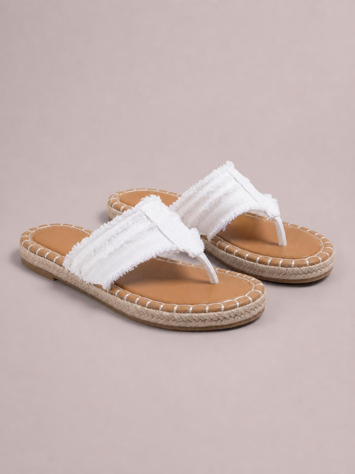 White canvas toe-post flat sandals feature frayed raw-hem straps, tan footbeds, and textured rubber soles with stitched edge detailing.